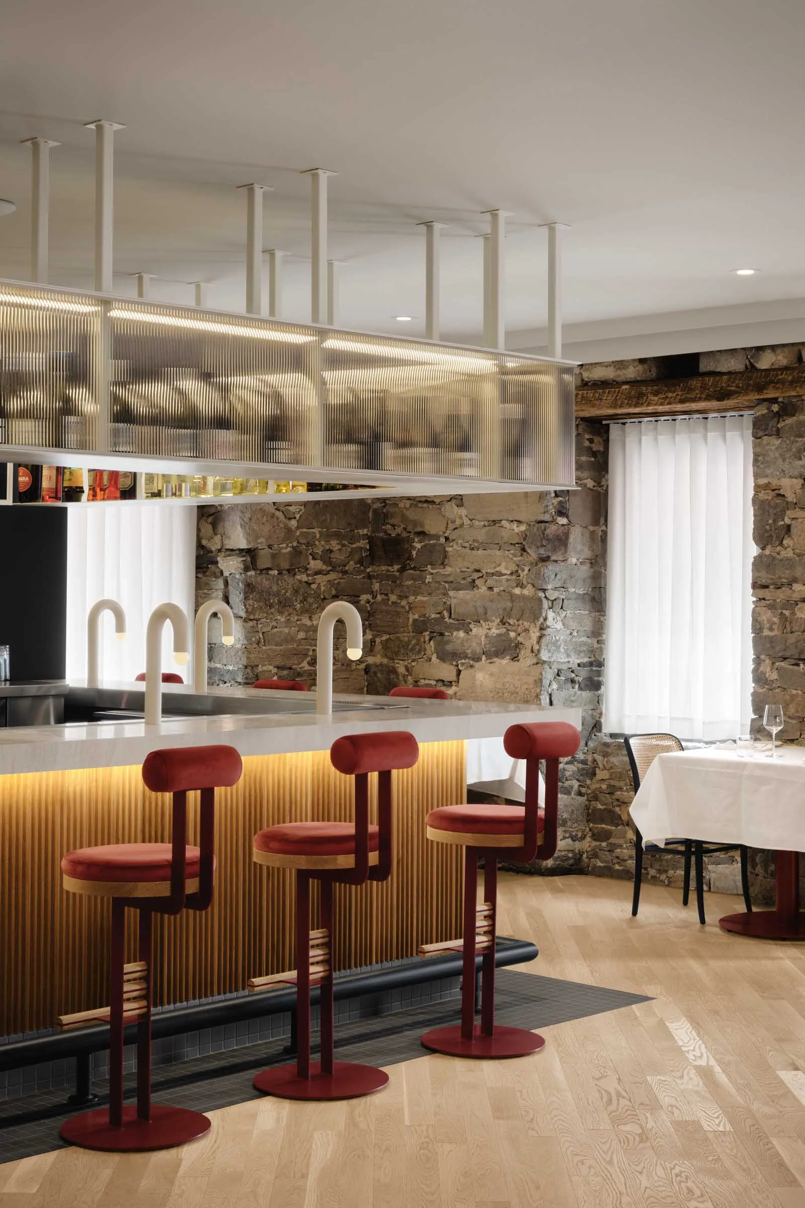 A modern restaurant bar featuring wood, glass, and stone materials with stylish red bar stools.