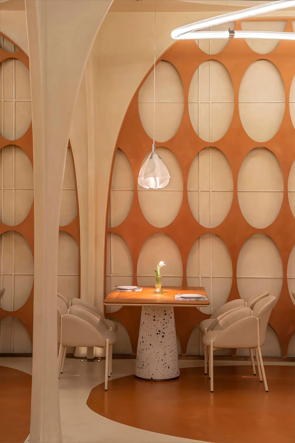 A modern restaurant interior featuring a table with a vase of flowers, surrounded by chairs on a terrazzo floor.