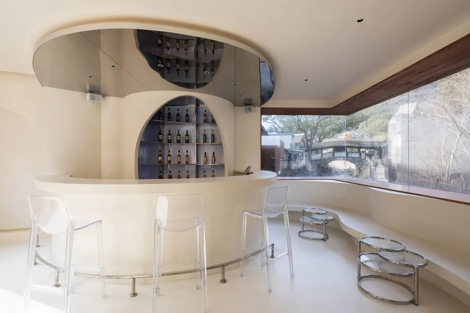 A minimalist bar with glass shelves and metal stools.