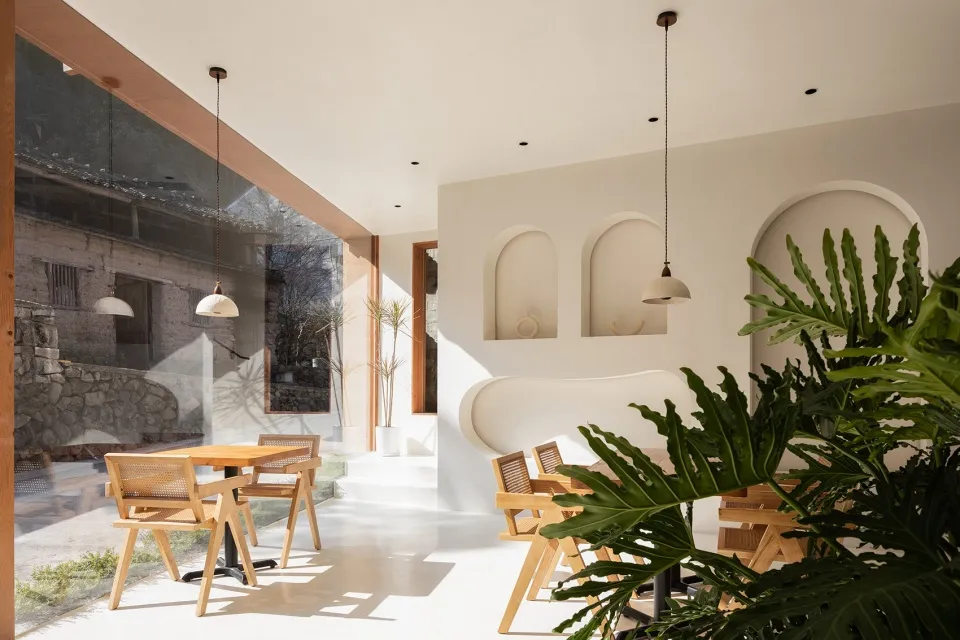 A modern cafe interior featuring mixed materials, with a focus on the light, airy ambiance created by the large windows and n