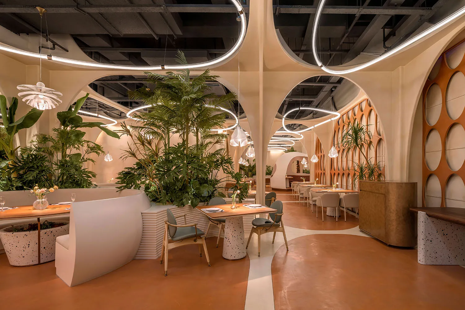 A modern restaurant interior with concrete finishes and white planters filled with greenery.