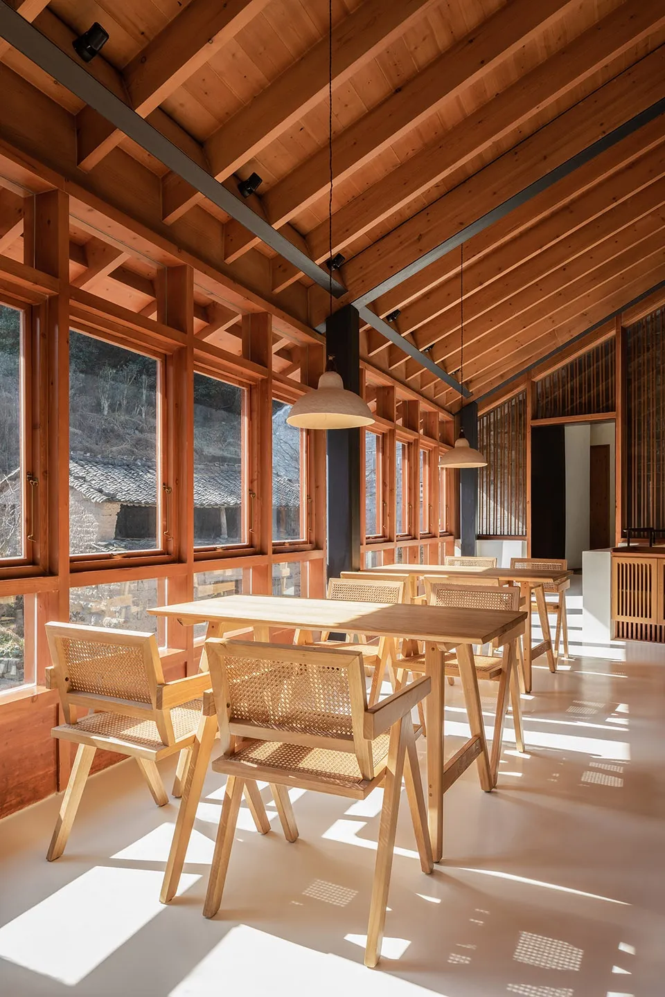 Modern restaurant interior with wooden tables and chairs, large windows, and natural light.