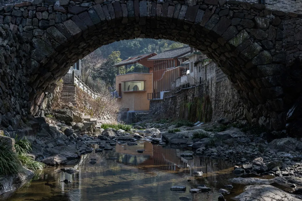 A stone bridge with an archway reflected in a calm waterway surrounded by natural elements.