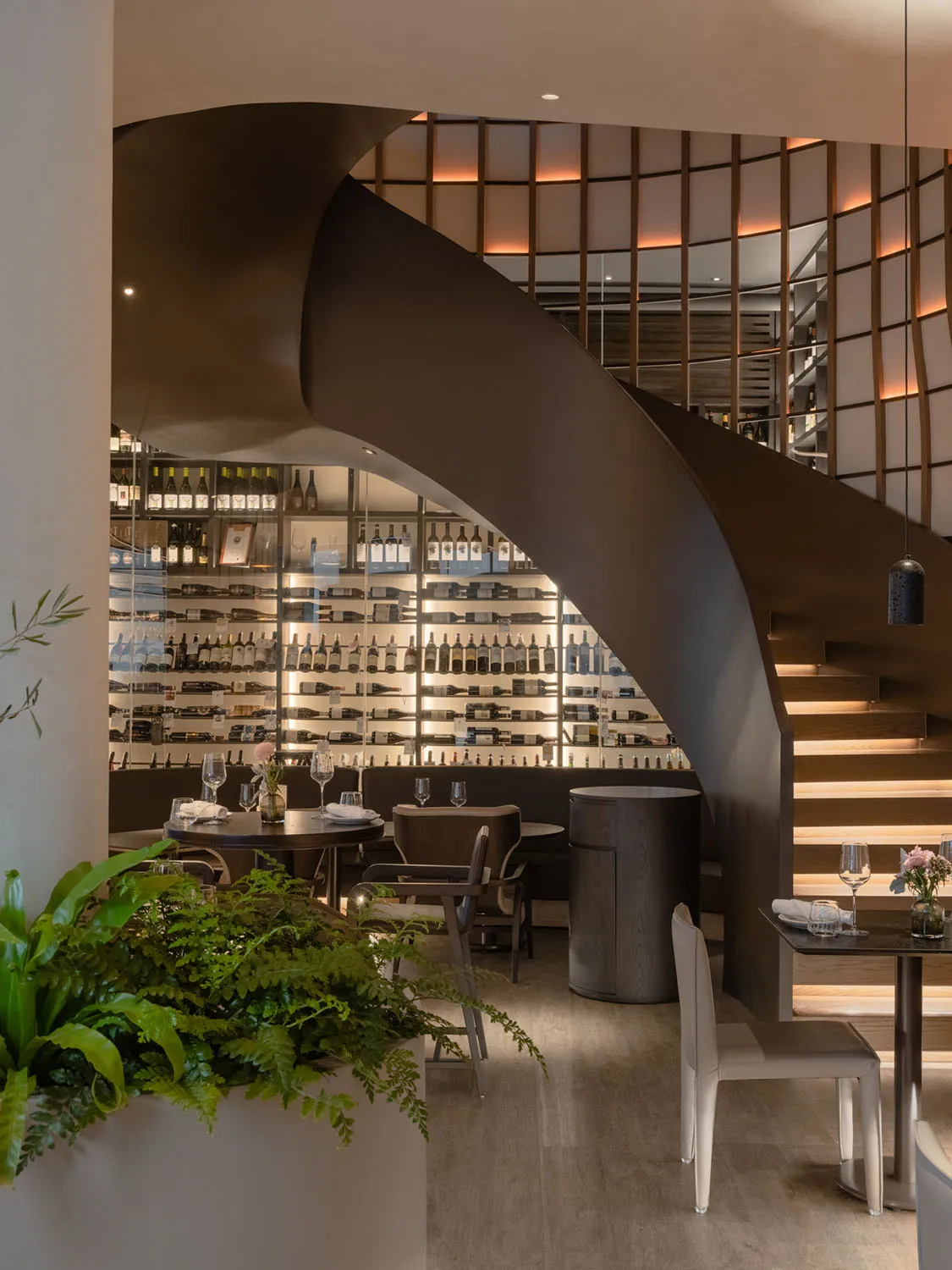 A modern restaurant bar featuring wooden materials and a spiral staircase with illuminated railings.