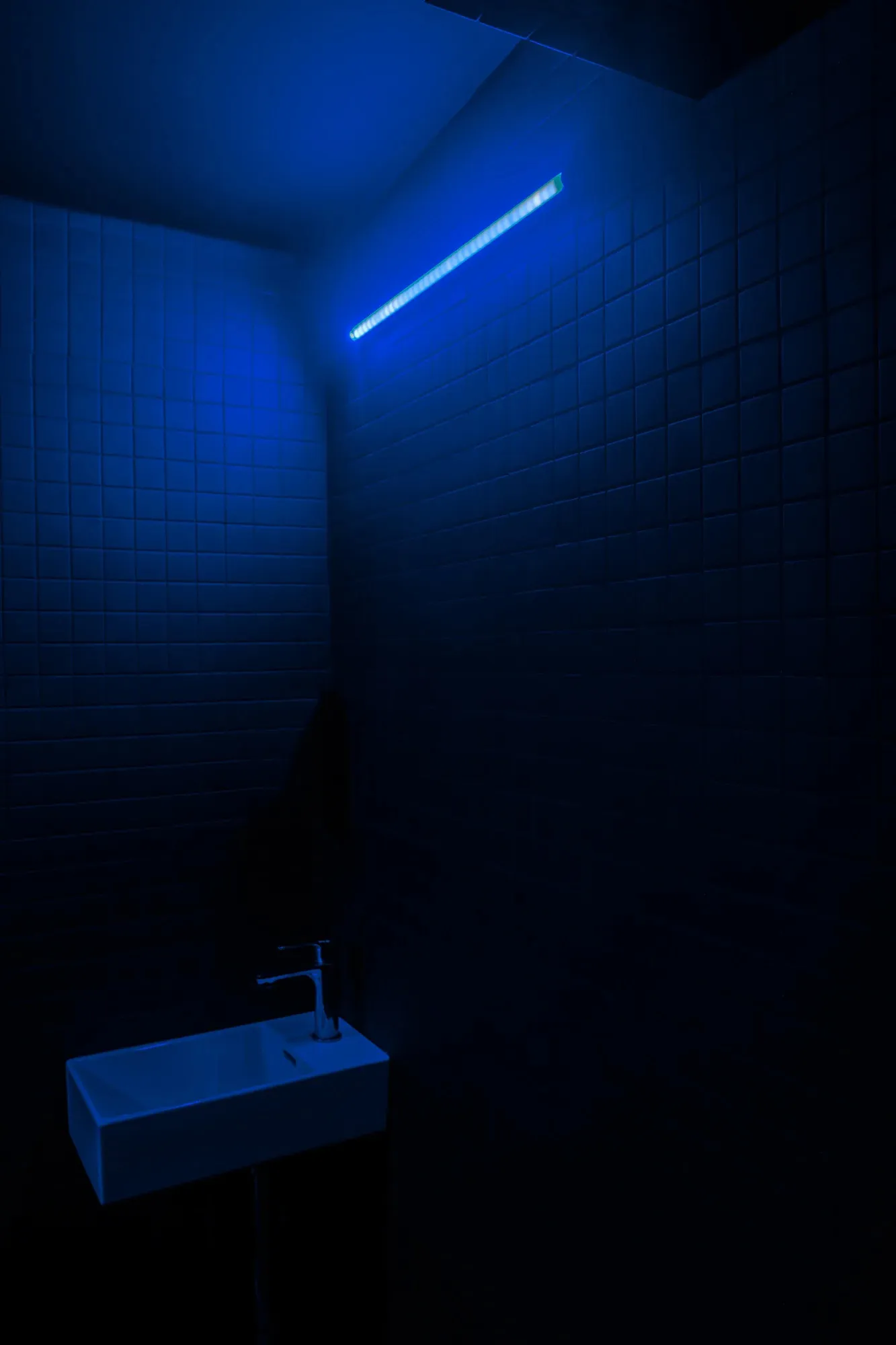A minimalist bathroom with blue lighting and tile walls.