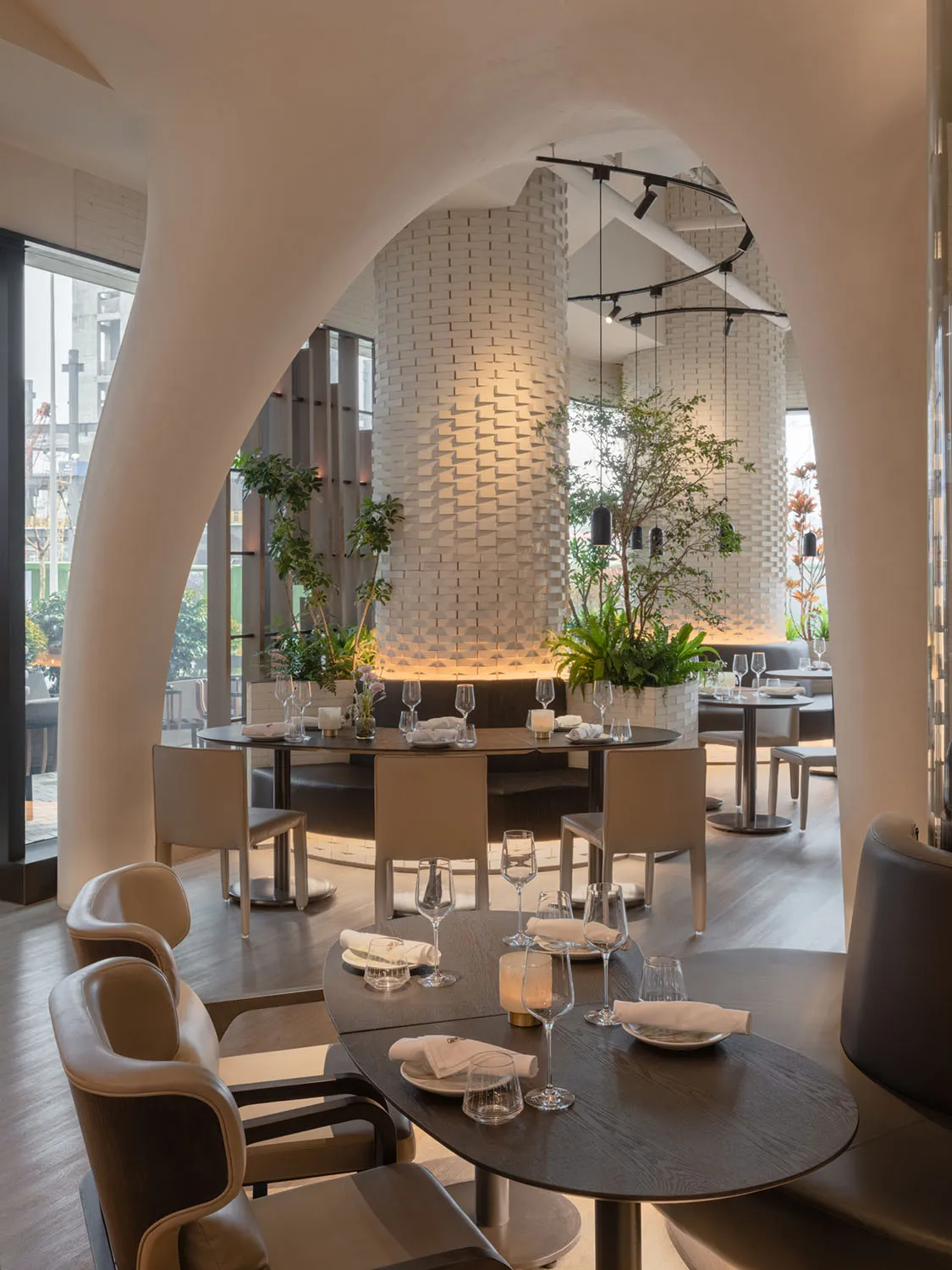 A modern restaurant interior featuring wooden tables, leather chairs, and indoor plants.