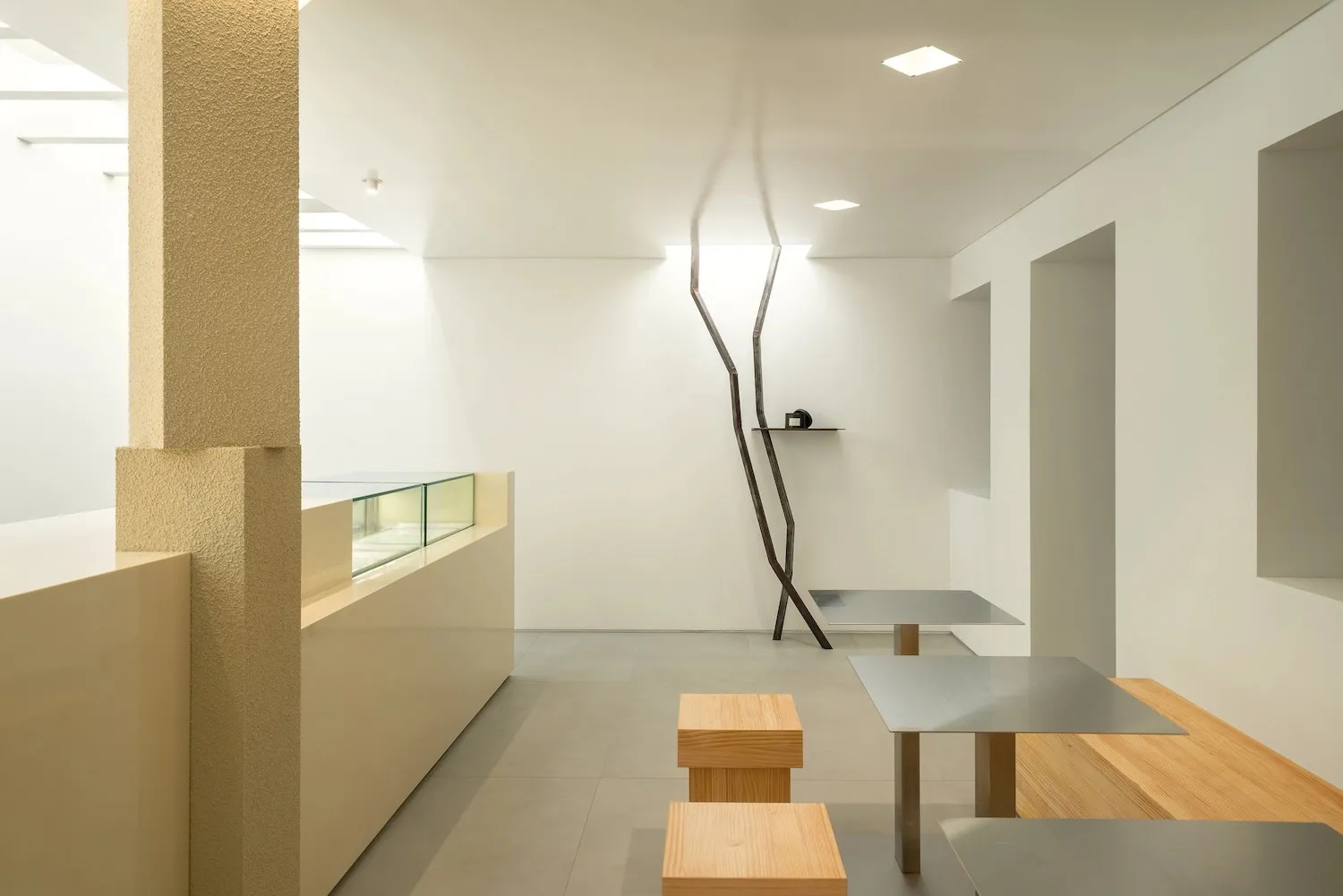 Modern restaurant interior with minimalist design featuring metal tables, wooden benches, and concrete flooring.
