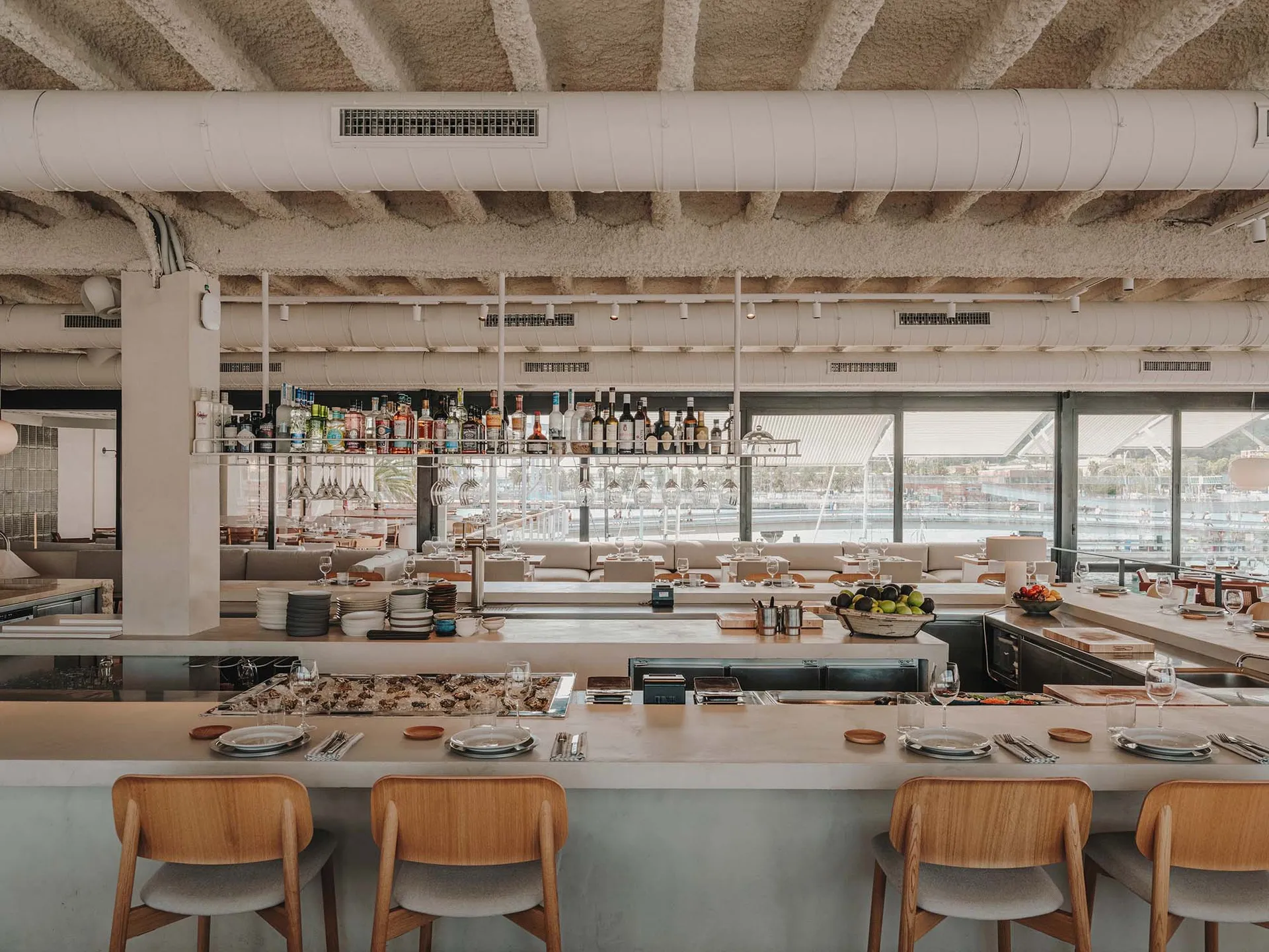 Industrial-style restaurant bar with concrete walls, open ceiling beams, and a range of drinks on the counter.
