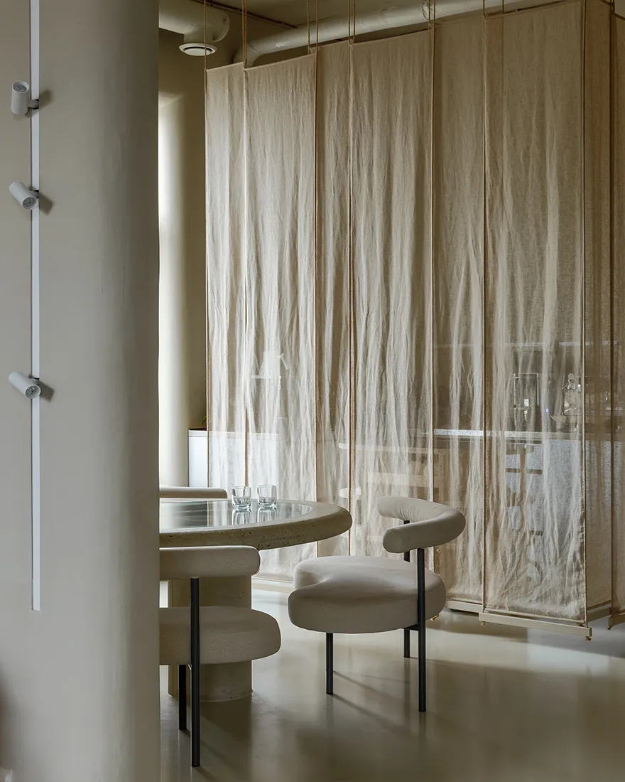 Minimalist restaurant interior featuring a round table, chairs, and fabric curtains.