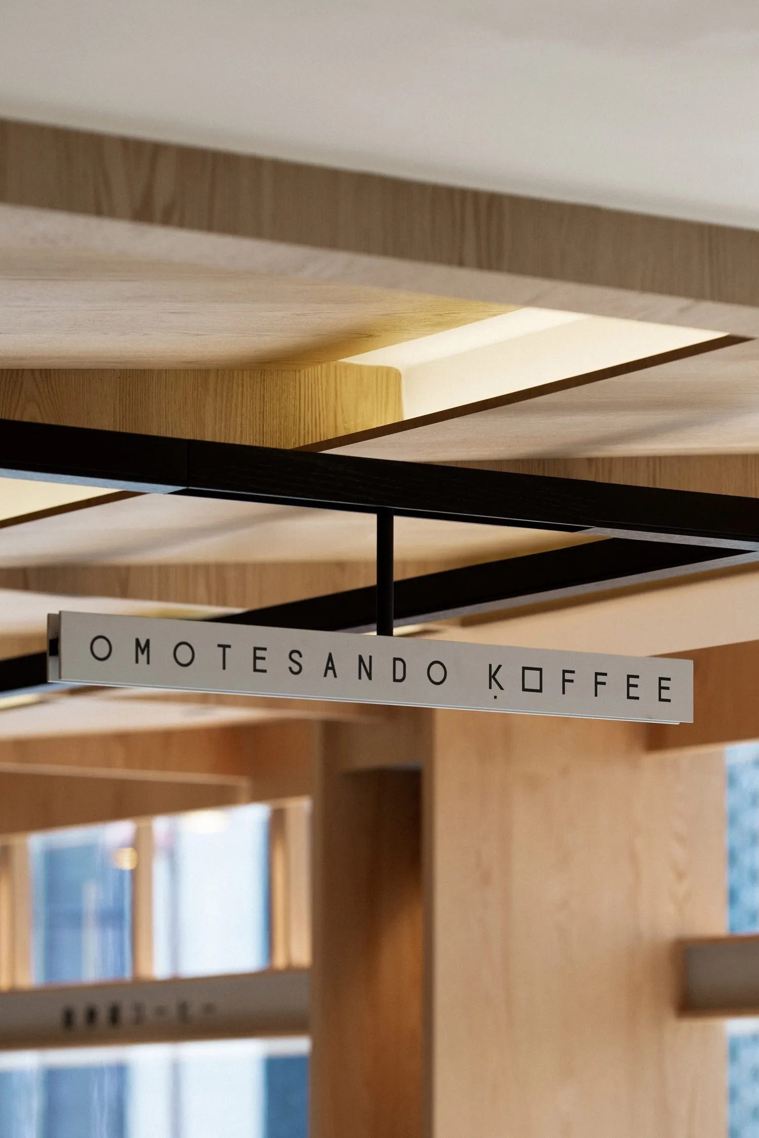 A modern coffee shop interior with a wooden sign that reads 'OMOTESANDO KOFFEE'.