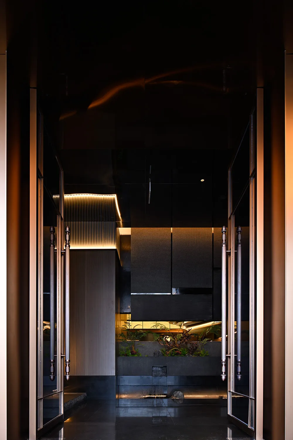 A modern entrance hall featuring glass walls, concrete flooring, and warm indoor lighting.