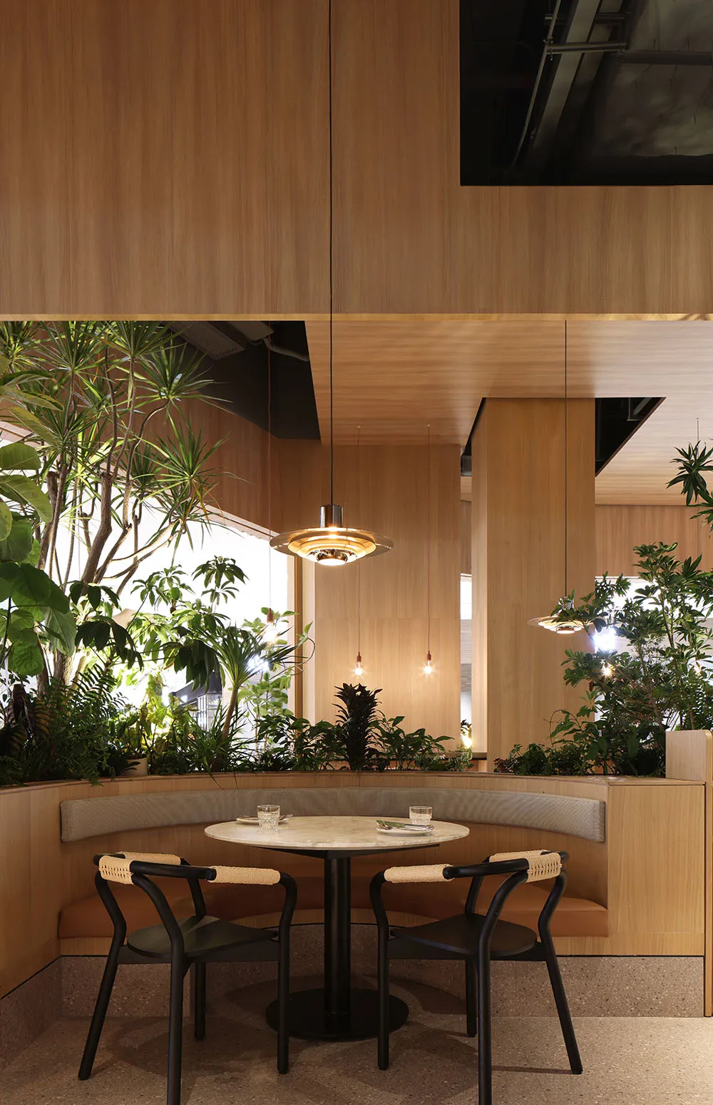 A cozy cafe interior featuring wooden walls and ceiling, plant decoration, and a round table with chairs.