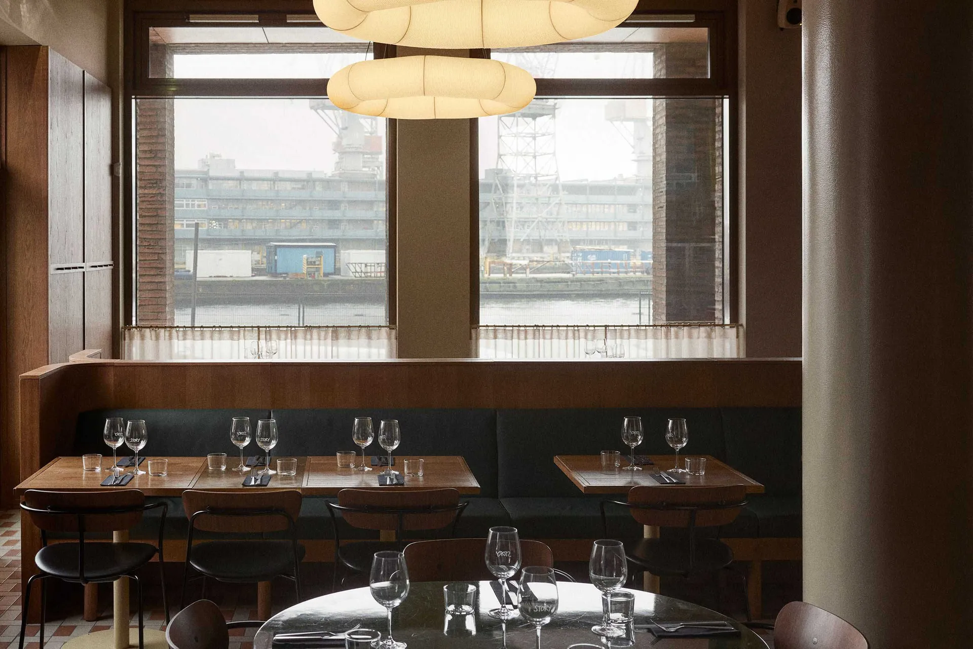 Modern cafeteria interior with wooden tables and chairs, large windows, and industrial-style lighting.