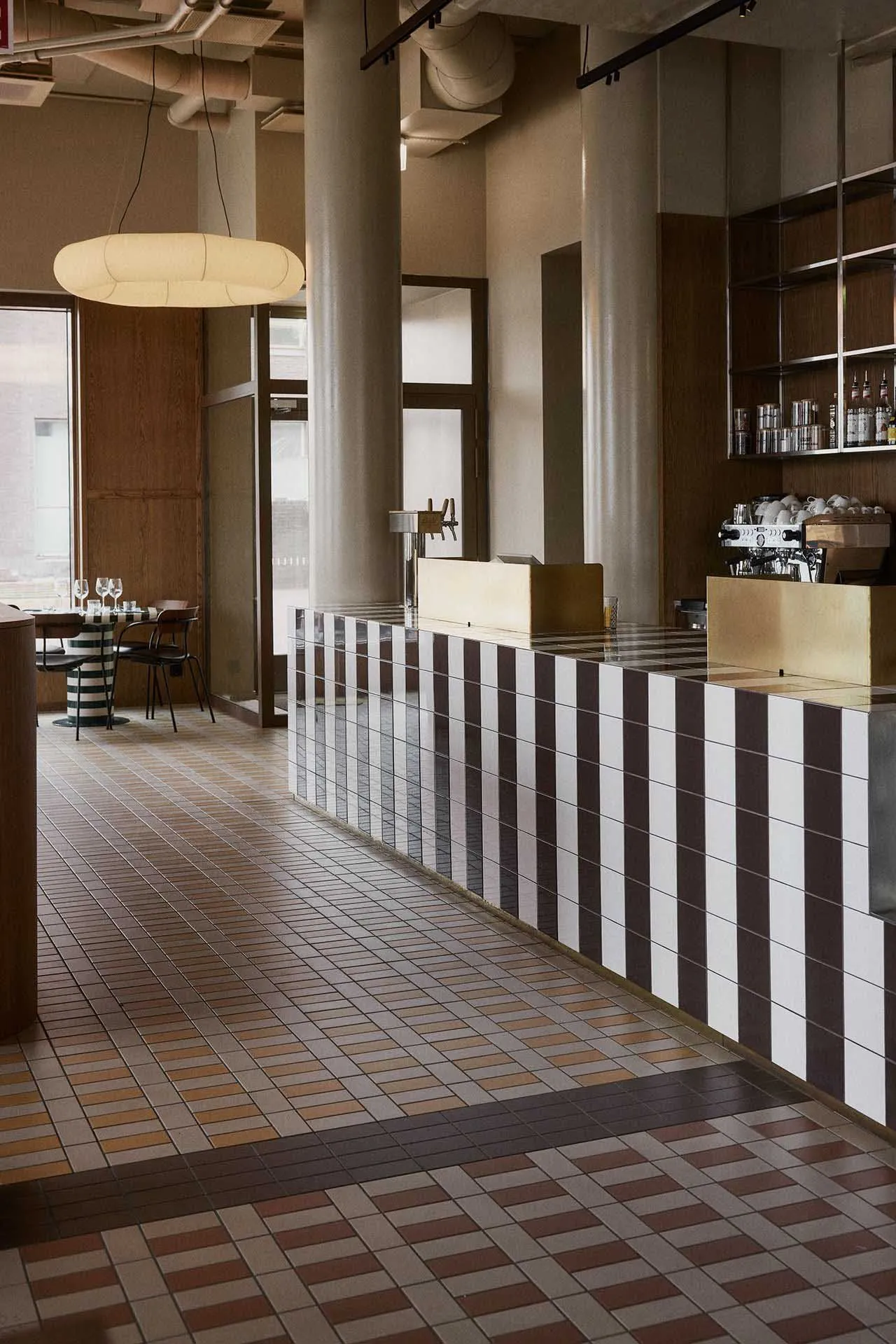 A minimalist coffee shop interior with a tiled counter and a modern hanging light fixture.