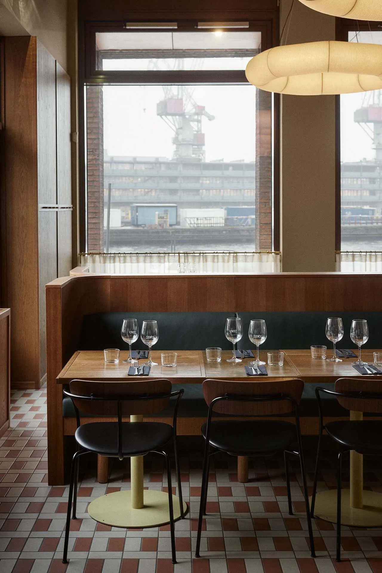 A modern restaurant interior with wooden tables, leather chairs, and large windows overlooking a harbor.