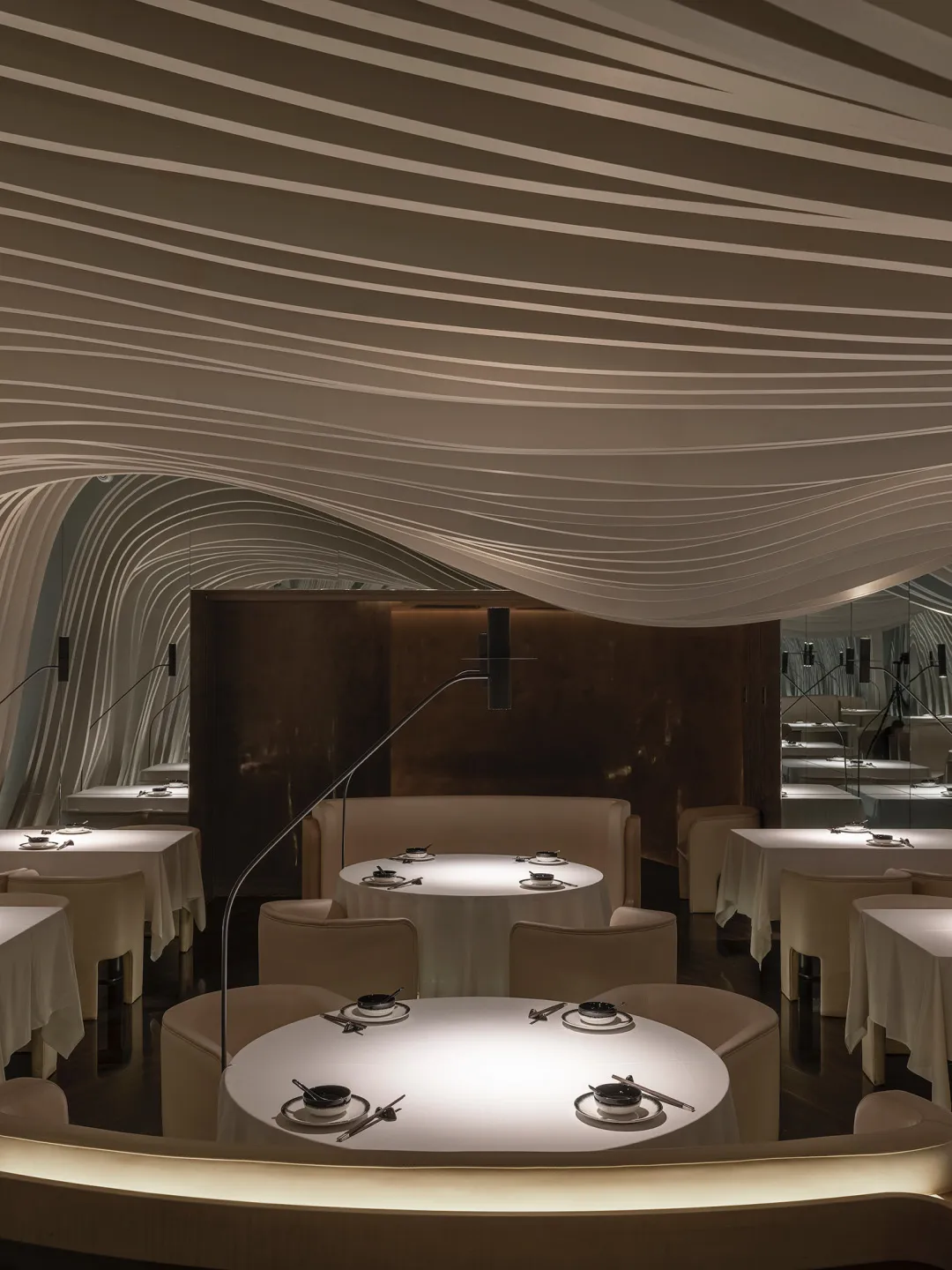 A modern restaurant interior with white textured fabric ceiling and round tables.