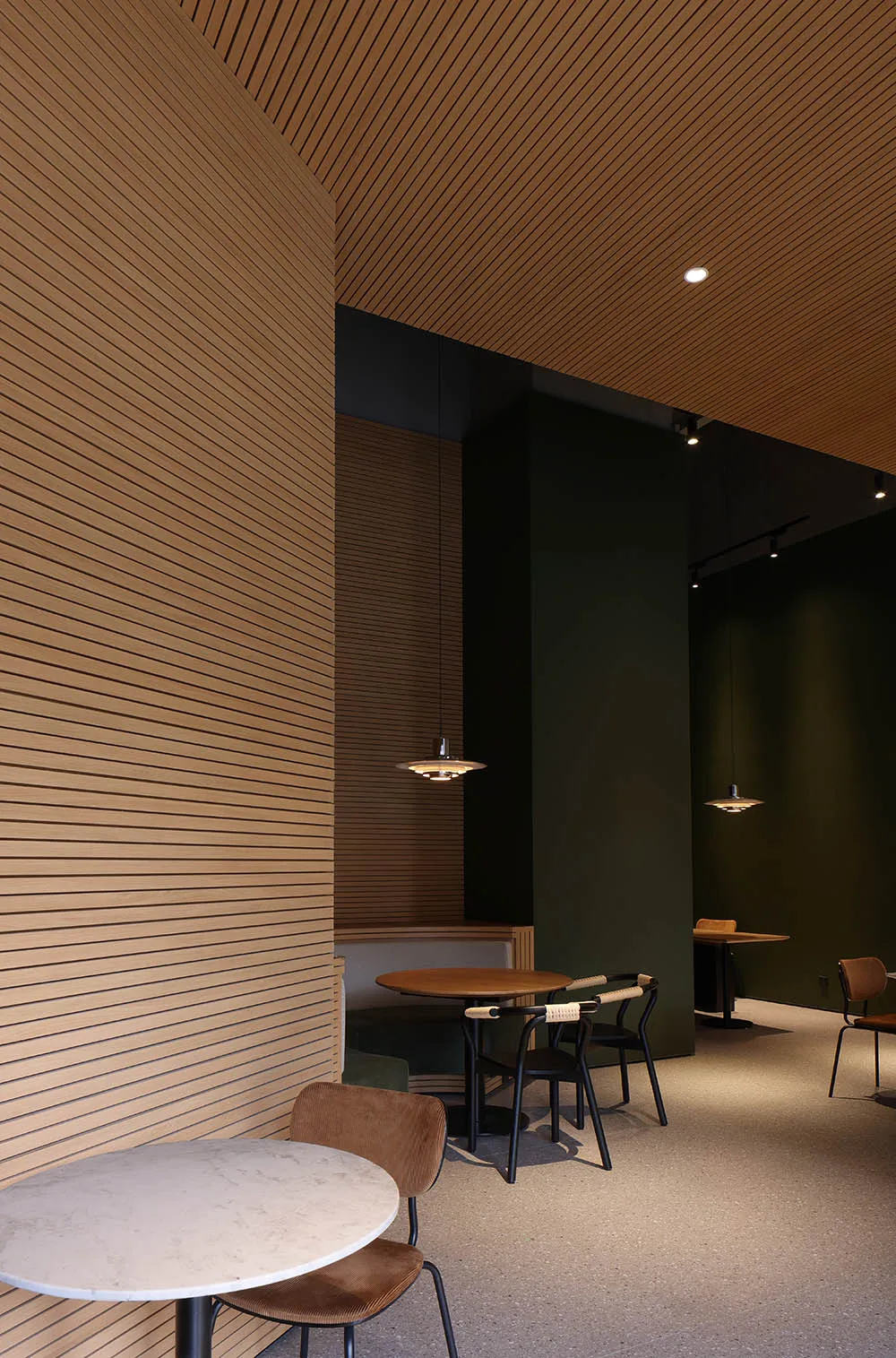 A modern restaurant interior featuring wooden walls and tables, minimalist furniture, and contemporary pendant lighting.