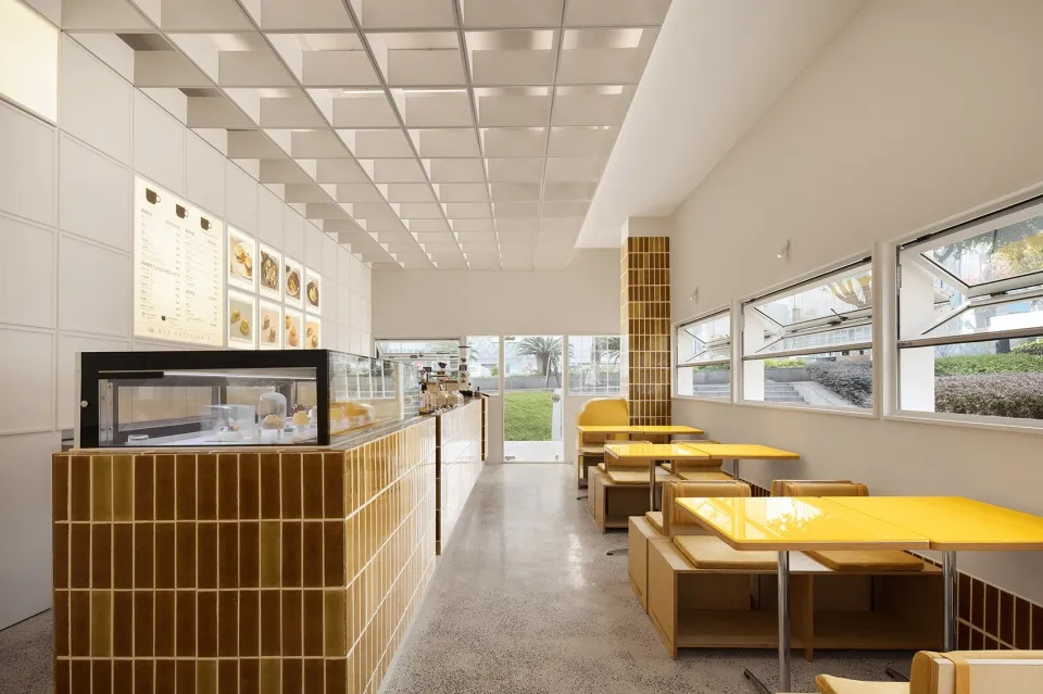 Modern minimalist cafe interior with yellow tiled bar counter and seating area with large windows and natural light