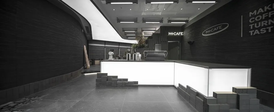 A sleek, minimalist coffee shop interior with a concrete counter and geometric design elements.