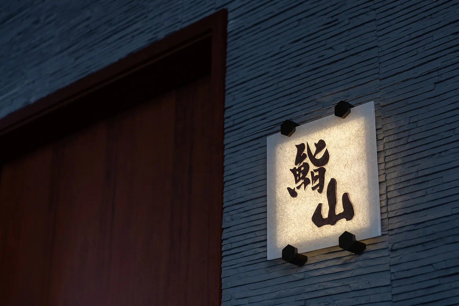 A modern restaurant signage with paper lightbox illumination displaying black characters against a wooden background.