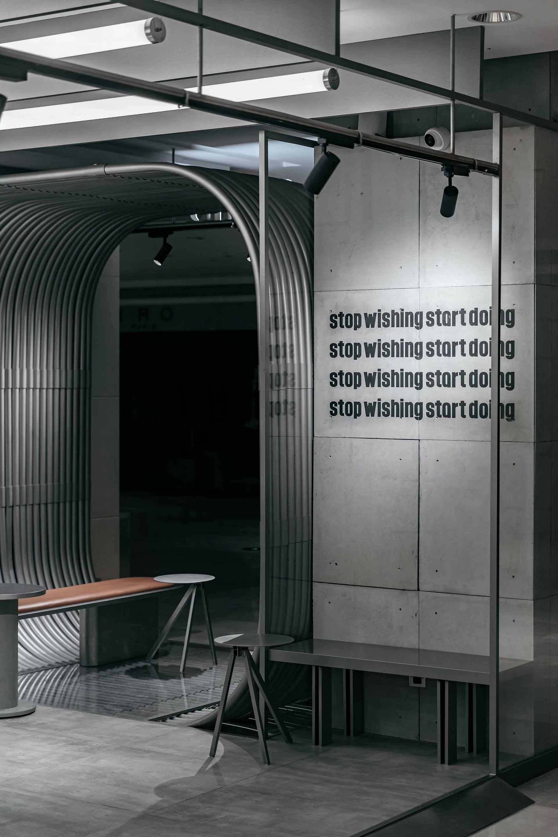 The minimalist café features concrete walls and a modern seating area with a glass enclosure.