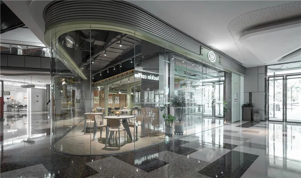 Modern minimalist coffee shop interior with glass walls, sleek tables, and white chairs.