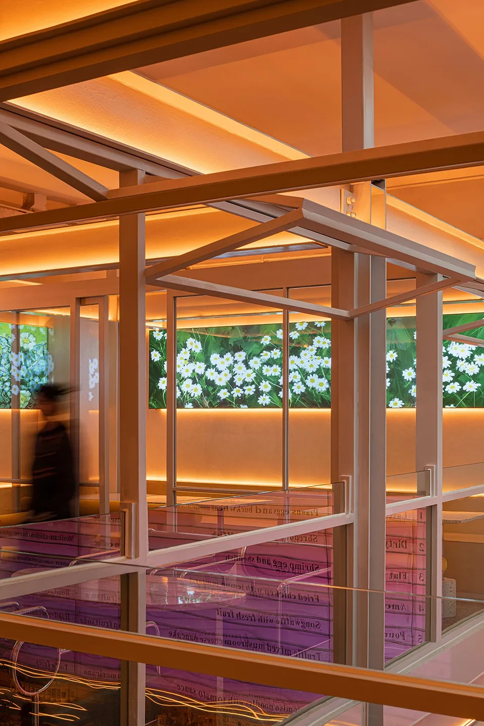 A modern restaurant interior with glass walls, metal framing, and a digital display showing flowers.