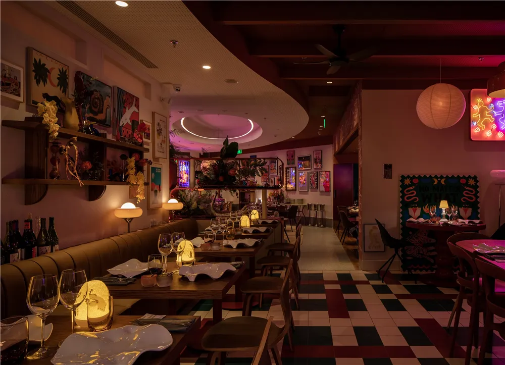 A beautifully designed restaurant interior with wooden furniture, checkered floor tiles, and colorful artwork on the walls.