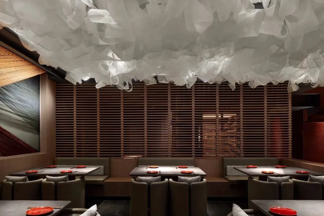 A modern restaurant interior featuring a white fabric ceiling, wooden slatted walls, and sleek seating.