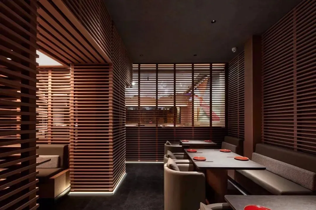 A modern restaurant interior with wooden paneled walls, white upholstered seating, and red plates on the tables.