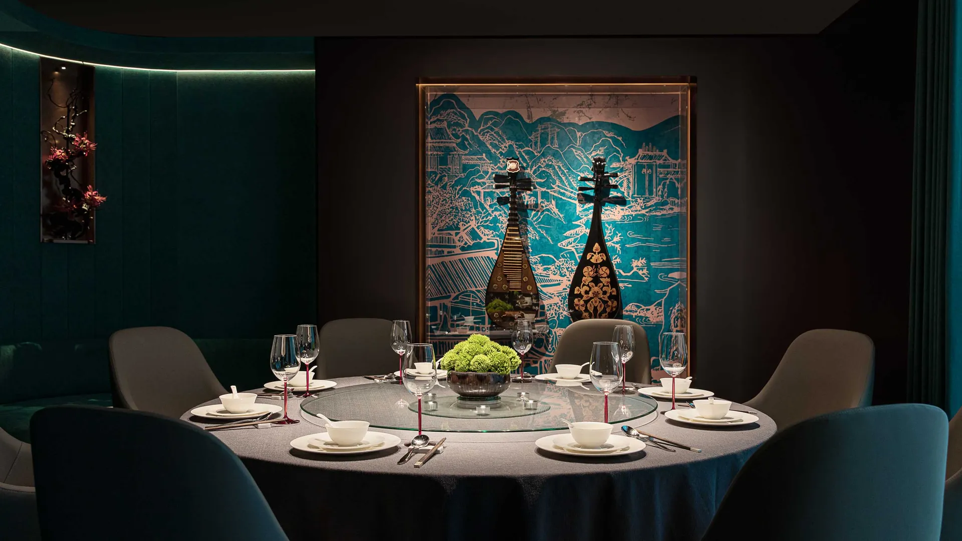 A round dining table set for six in a restaurant dining room, featuring a textured wall covering, glass tabletop, and upholst