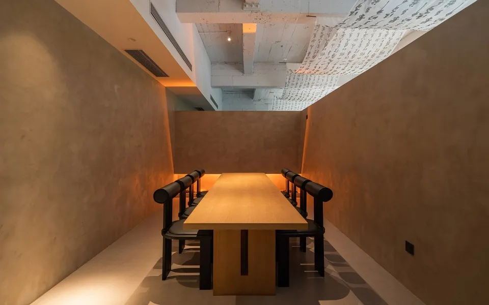 A spacious, industrial-style conference room featuring a long wooden table surrounded by black chairs.