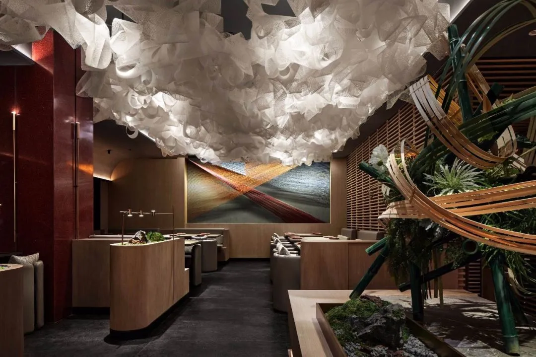 Modern restaurant interior with a white organic cloud ceiling, bamboo structure, and a waterfall fountain centered on a red a