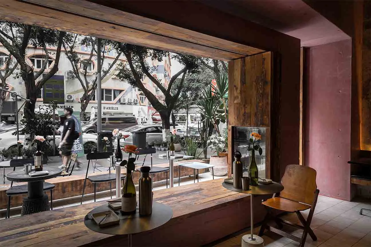 Interior view of a cafe bar with wooden tables, chairs, and decorations, with street view seen through a window.
