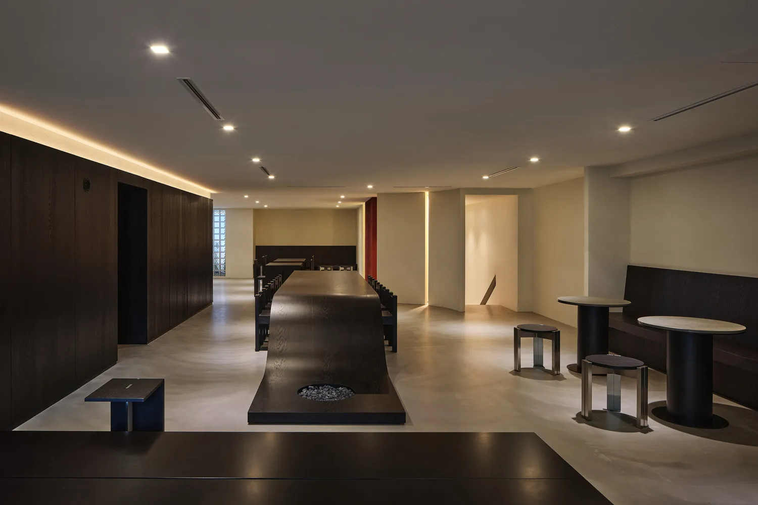 A minimalist lounge area featuring a large concrete table and seating arrangements, with warm lighting and modern design elem