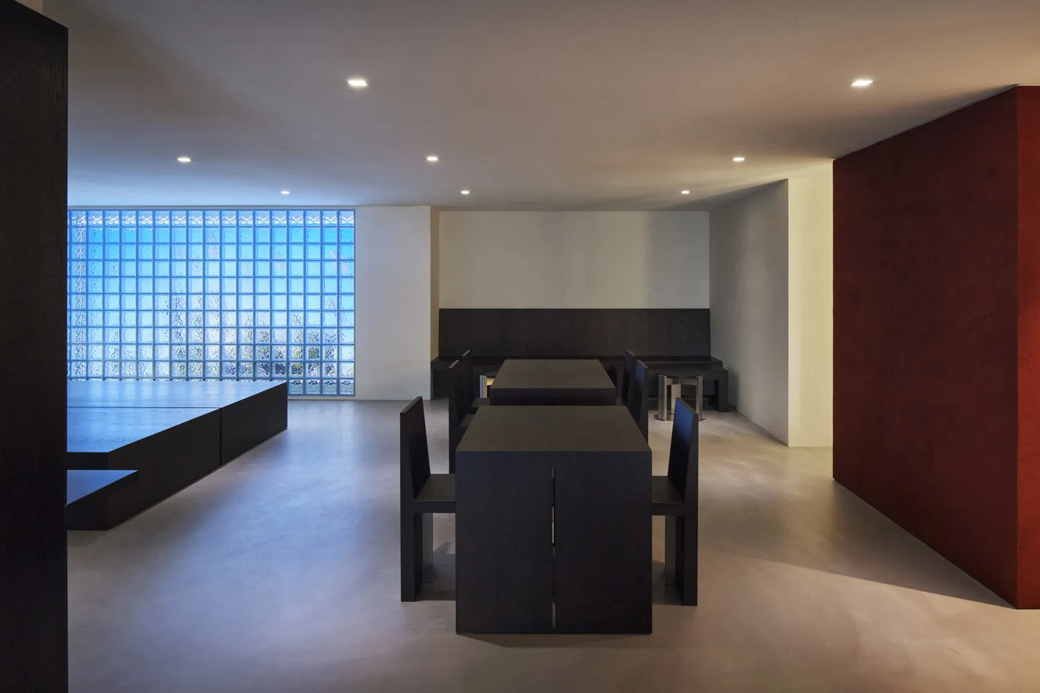 Modern dining room interior with dark wooden furniture against a white wall, featuring a glass-block wall.