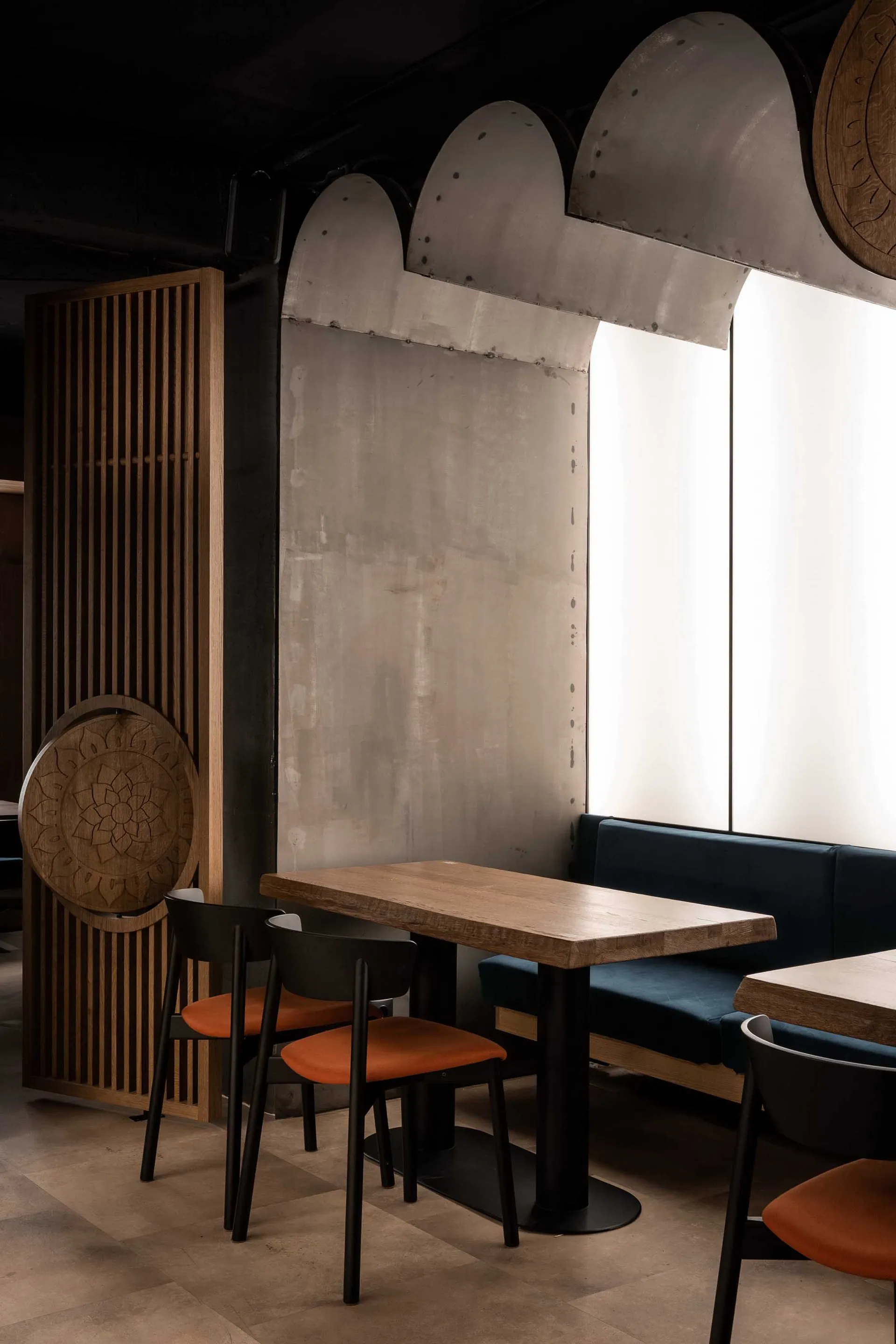 Modern restaurant seating area featuring wooden tables, concrete walls, and metal accents.