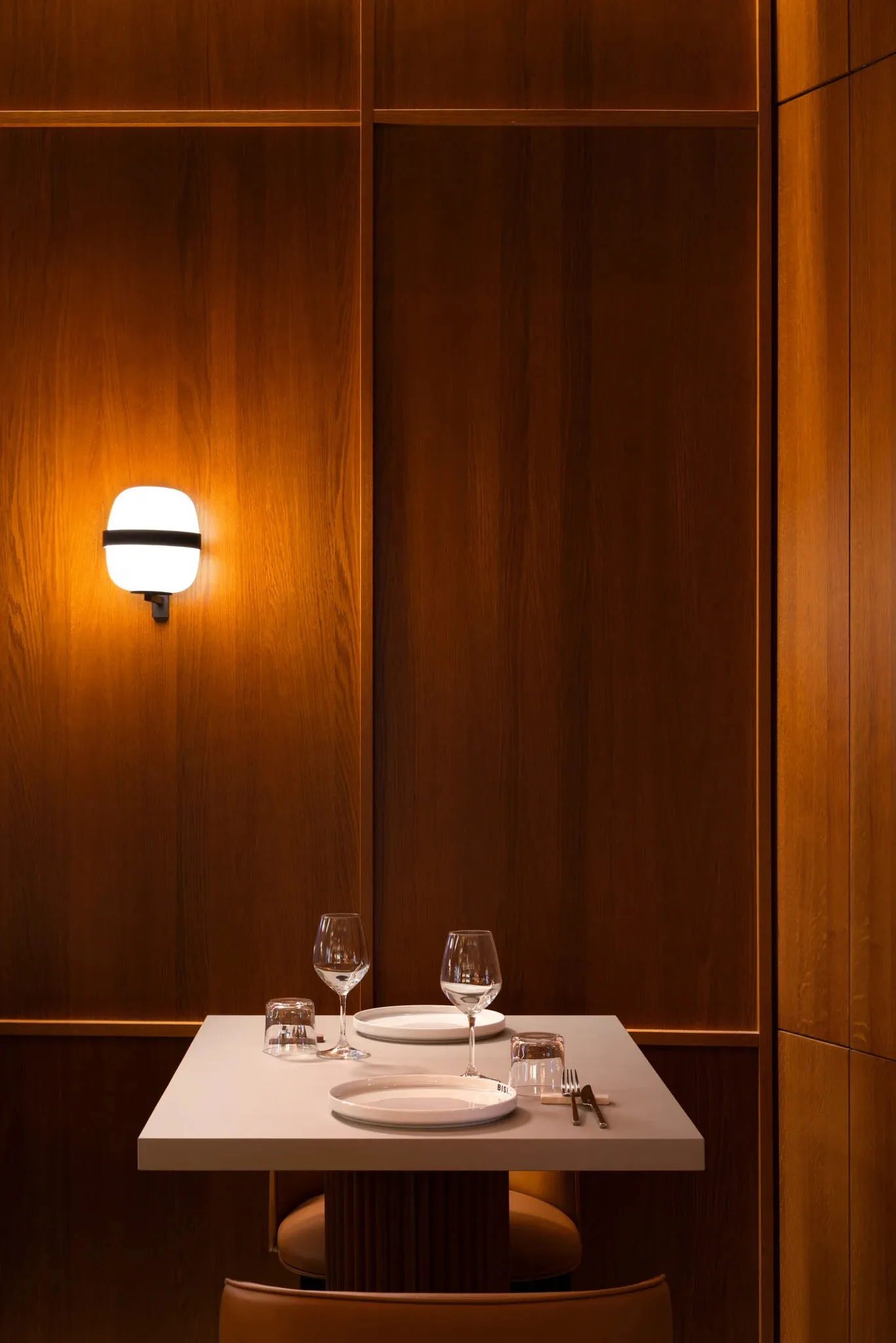 A minimalist restaurant interior with wood paneling and a table setup for a meal.