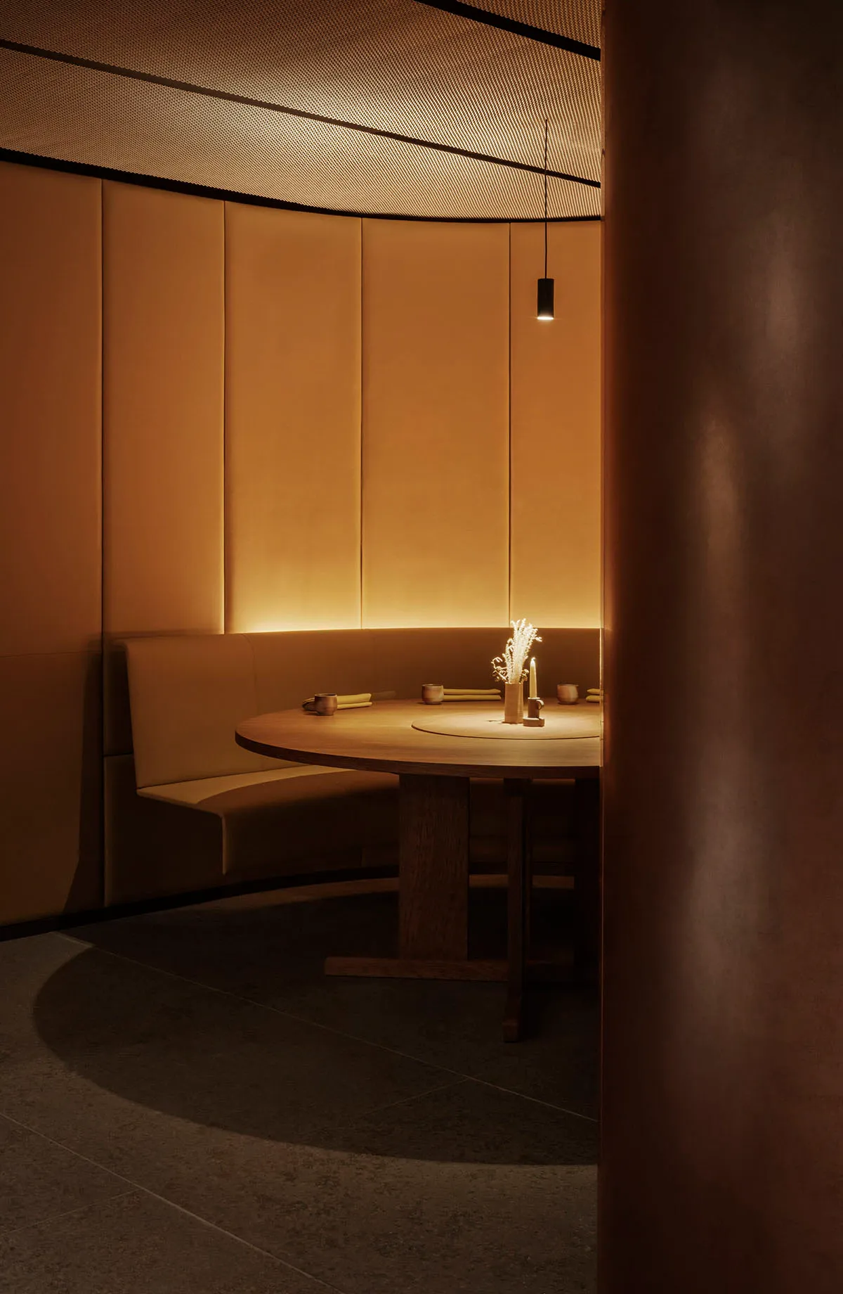 A minimalist restaurant dining room with a round wooden table, leather seating, and warm lighting.
