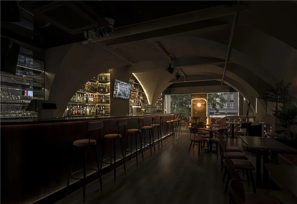 A modern bar interior with wooden and concrete materials and high stools at the bar.