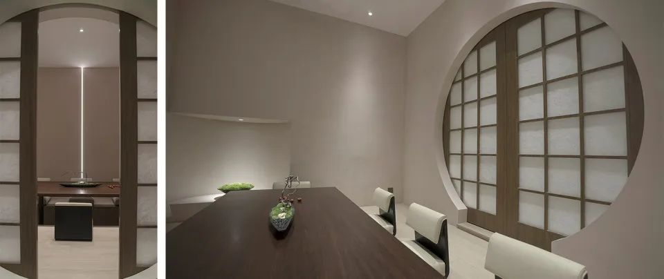 A minimalist dining room with white walls, wooden flooring, and a long wooden dining table.