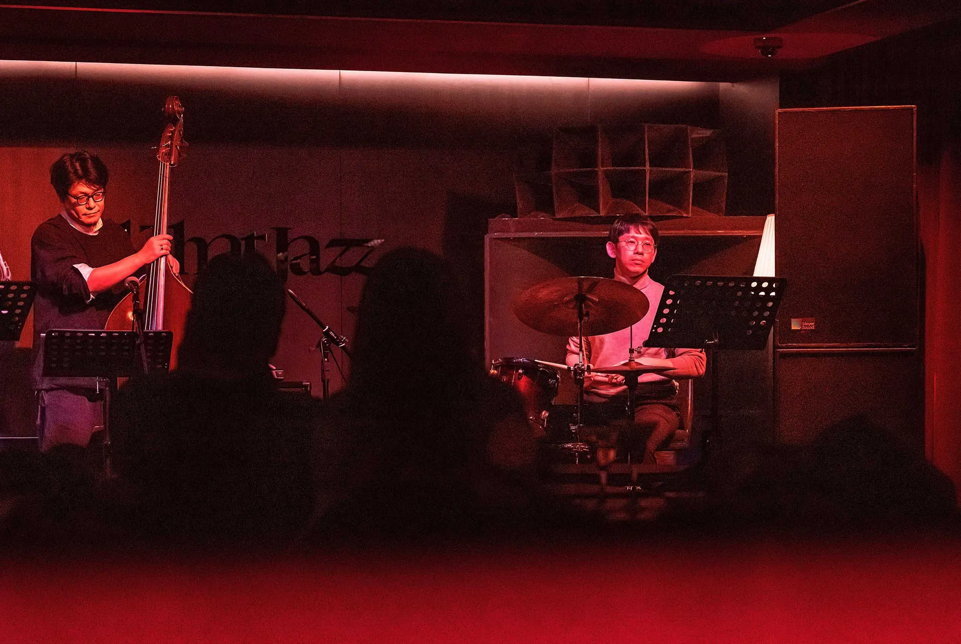 A jazz drummer and bassist performing on stage with a microphone and sound equipment.