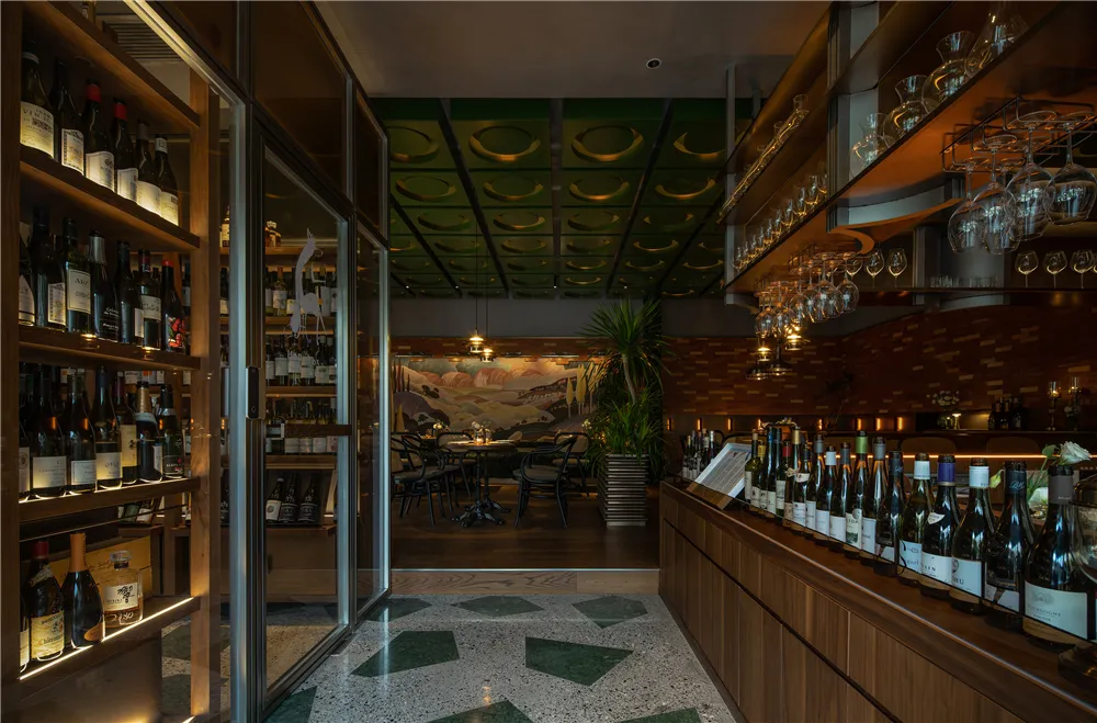 Modern wine bar interior with a glass-fronted shelf displaying wine bottles, a bar counter adorned with numerous wine bottles
