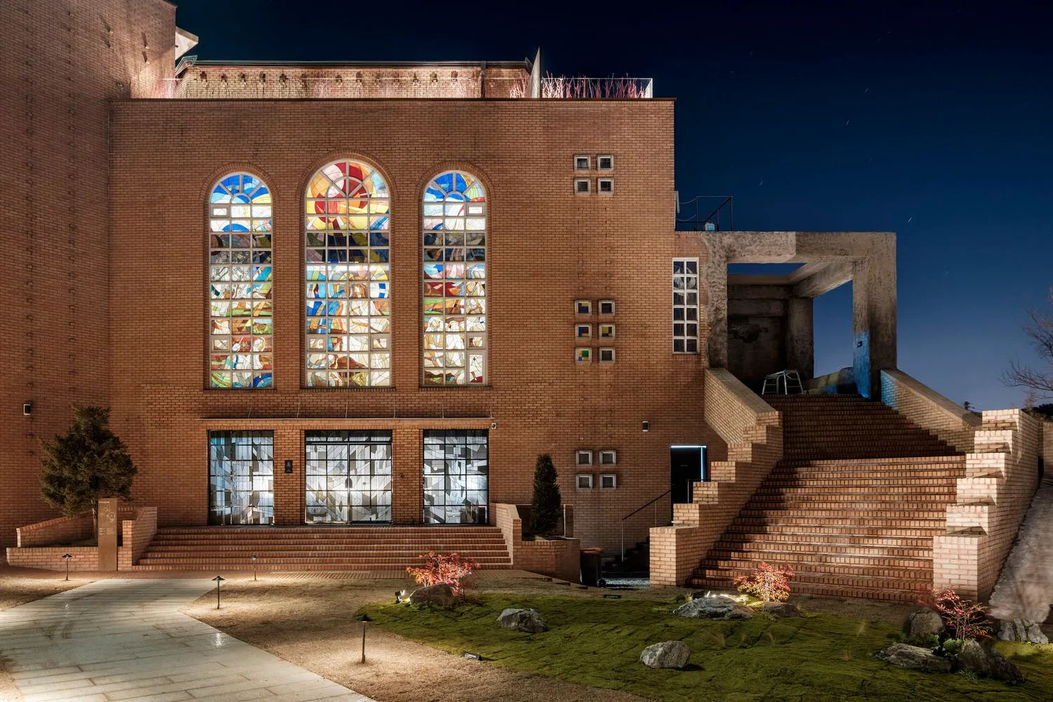 A modern building with stained glass windows made of red bricks and green moss.