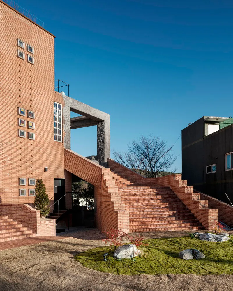 A modern building facade featuring a brick exterior with concrete structural elements and a garden area with steps and plants