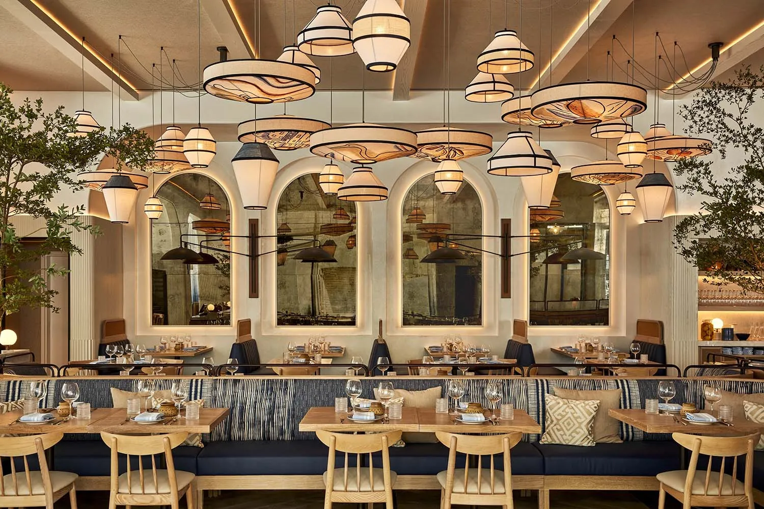 A modern restaurant interior with wooden tables, upholstered benches, and hanging pendant lights.