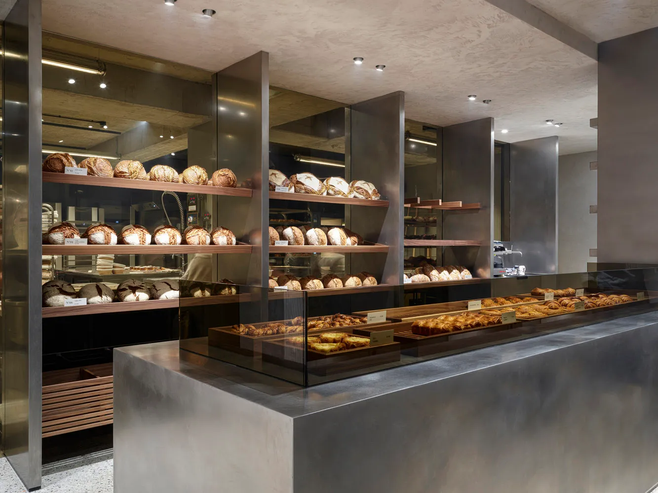 Modern bakery shop interior featuring glass display cases and metal shelving.