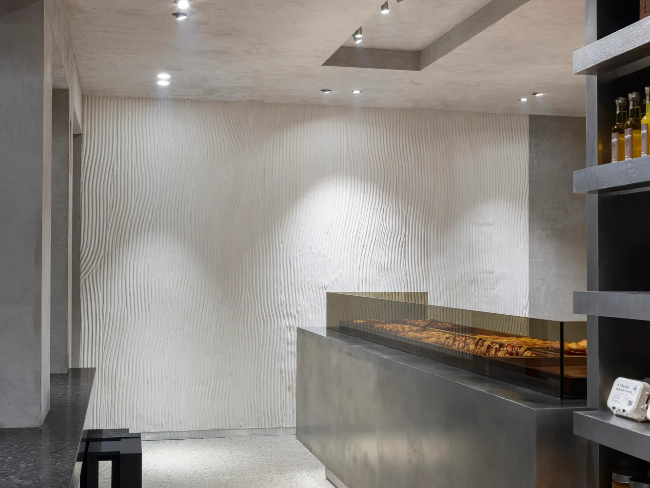 A modern, minimalist restaurant interior featuring concrete walls and flooring.