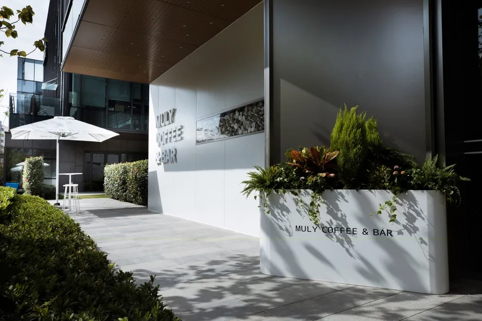 The exterior of a minimalist coffee bar with concrete walls and greenery.