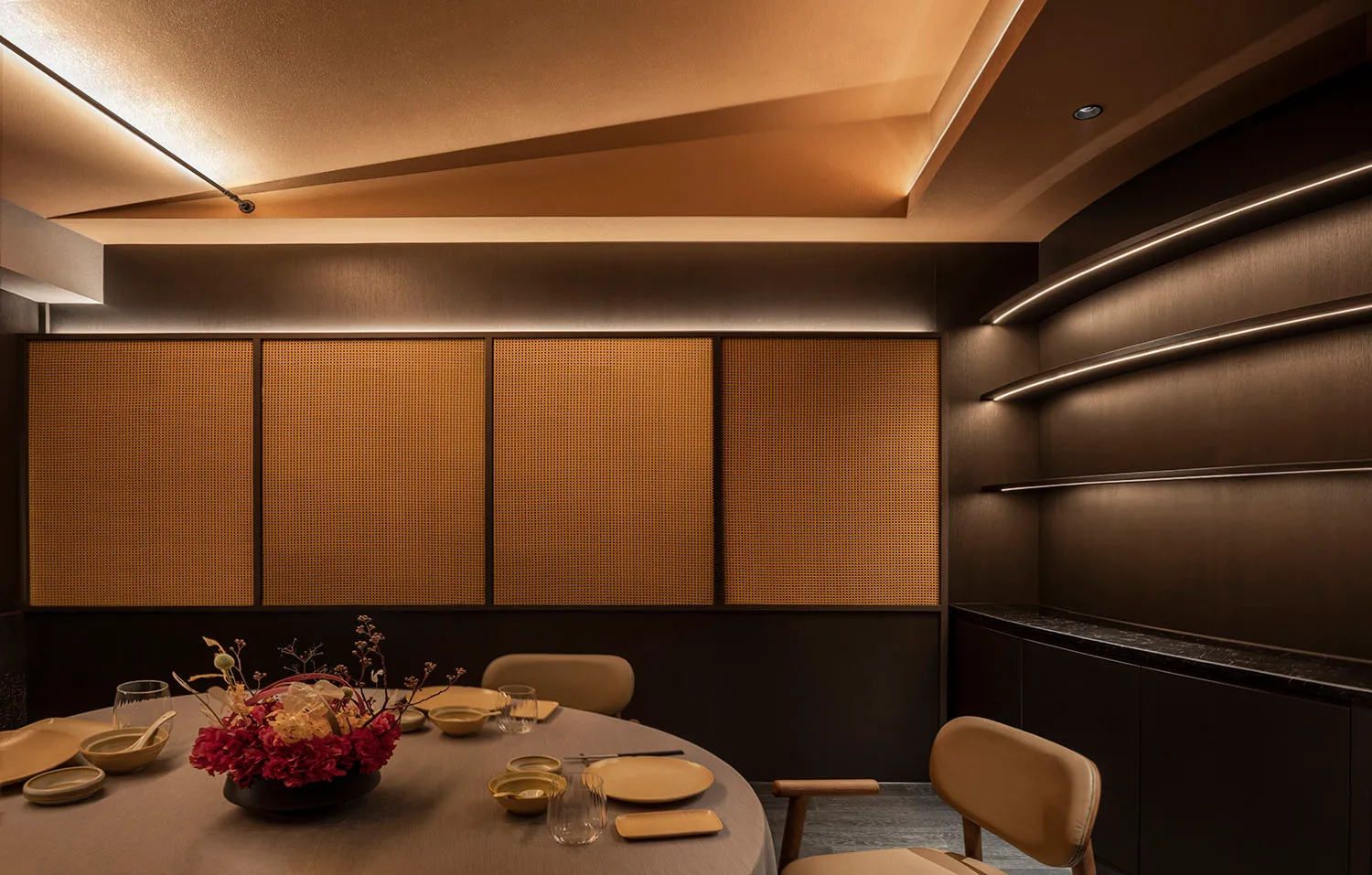Modern restaurant interior design featuring wooden paneling, round table with plates, glasses, and floral centerpiece.